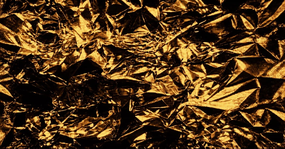 Close-up of densely crumpled reflective foil with sharp folds, deep creases, and overlapping angular facets filling the frame.